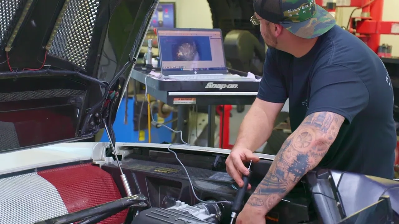 A Silver Arrow technician checking a scan tool laptop beside an open engine bay