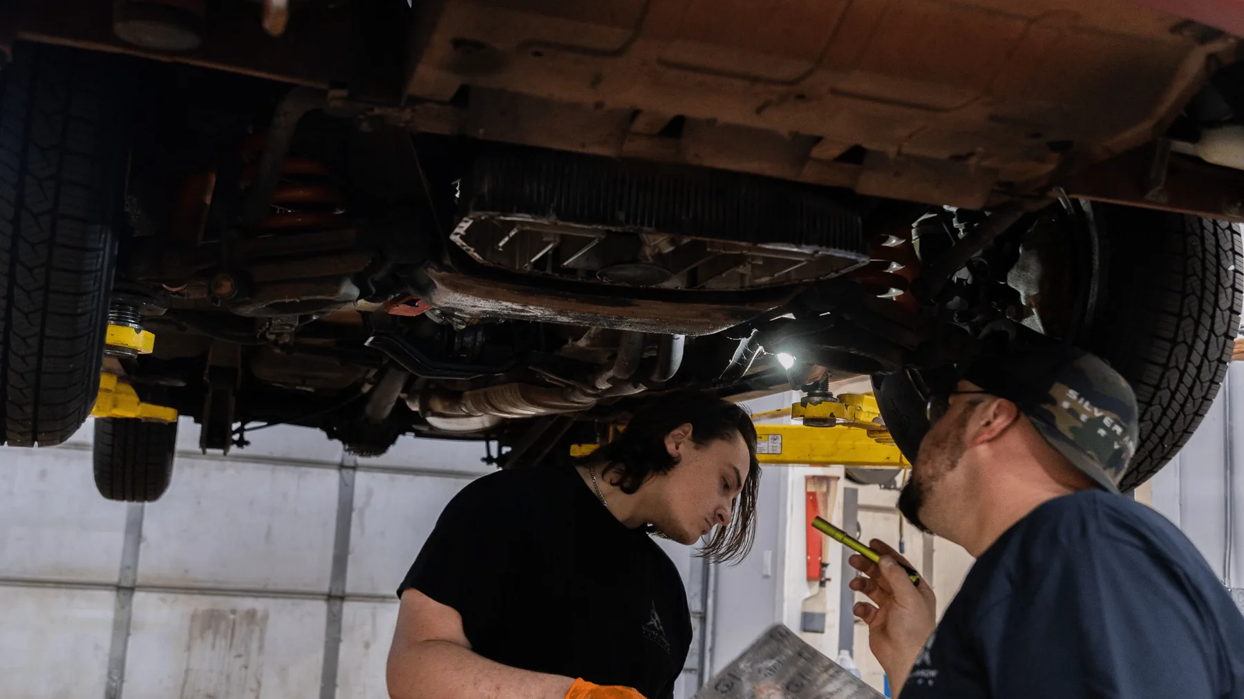 Two Silver Arrow technicians looking over the underside of a car on the lift